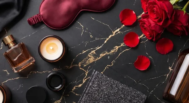 Set de cuidado de piel premium en mármol negro: frasco ámbar, perfume, velas encendidas, antifaz de seda y rosas rojas.